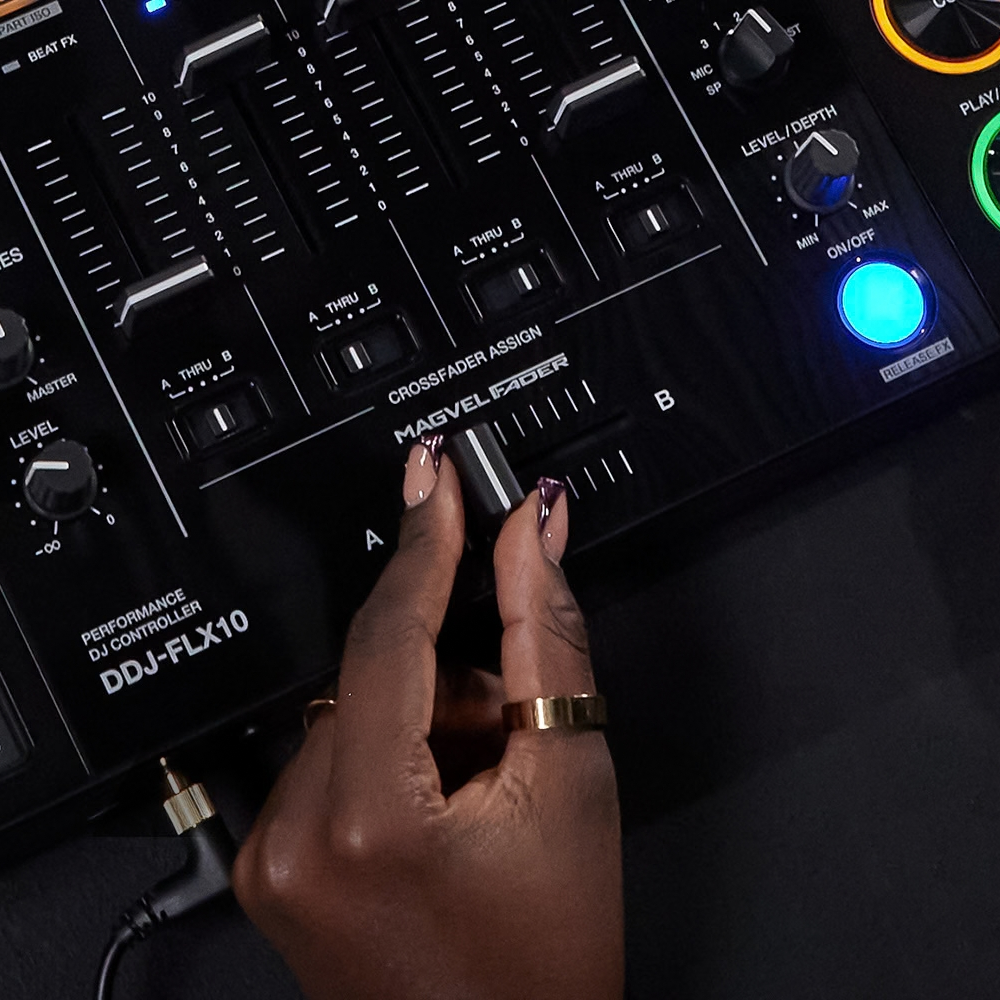 Close-up of a DJ adjusting the MAGVEL crossfader on the Pioneer DDJ-FLX10, with channel faders and effects controls visible.